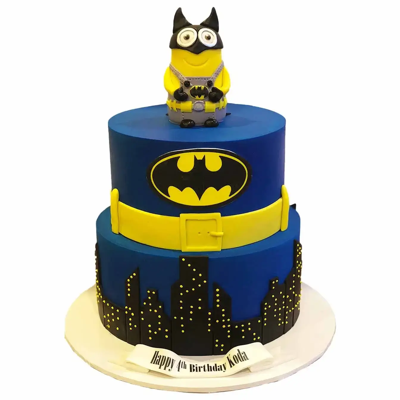 Batman Minion Adventure Cake - A two-tier cake with a cutout Gotham City skyline on the bottom tier and a minion on top dressed as Batman, a playful centerpiece for superhero-themed celebrations.