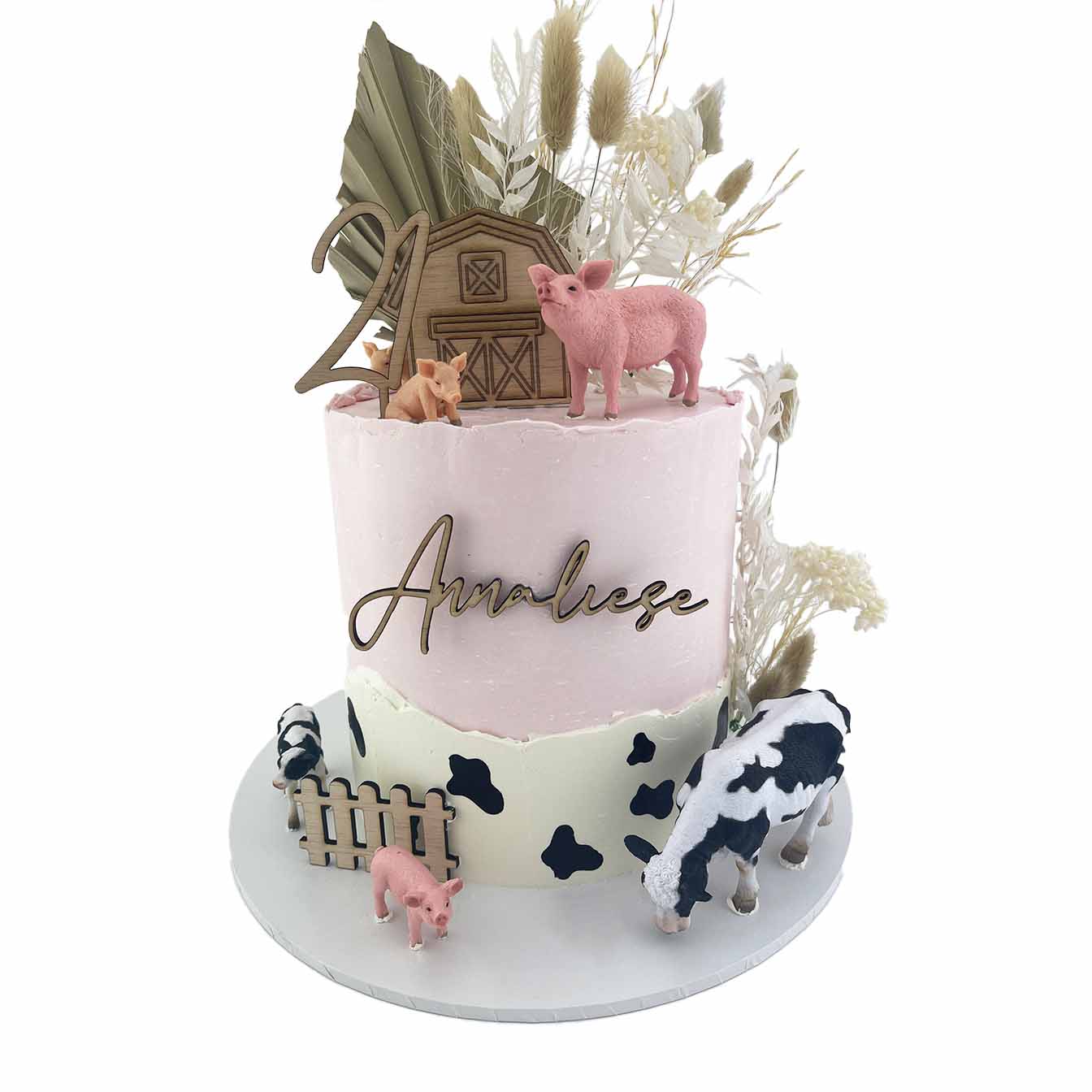 Pretty Barnyard Celebration Cake - A pink iced cake with hand-painted cow spots, wooden fence and barn toppers, pig and cow figurines, and dried flowers, a heartwarming centrepiece for a farm-themed celebration.