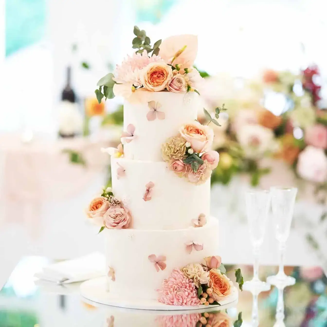 Floral Harmony Wedding Cake - A three-tier cake with scattered dried hydrangeas, fresh flowers, and molded roses on an ivory base, a breathtaking centerpiece for weddings filled with sophistication and natural grace.