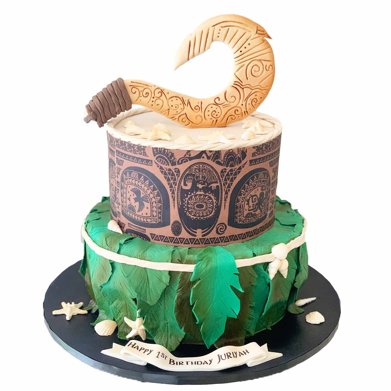 Maui's Hook Adventure Cake - A 2-tier cake featuring a moulded hook from Moana and an image wrap of Maui's tattoos, with palm leaves and shells on the base tier, a captivating centrepiece for a Polynesian-inspired celebration.
