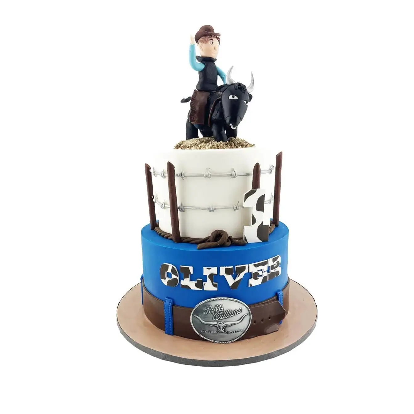Rodeo Roundup Cake with Bucking Bull and Belt Buckle - 2-tier cake with a white top tier featuring a barbed wire fence and a fondant-sculpted bucking bull, and a blue bottom tier that looks like a pair of jeans with a brown leather belt and a silver belt buckle customized with the child's name in cow print.