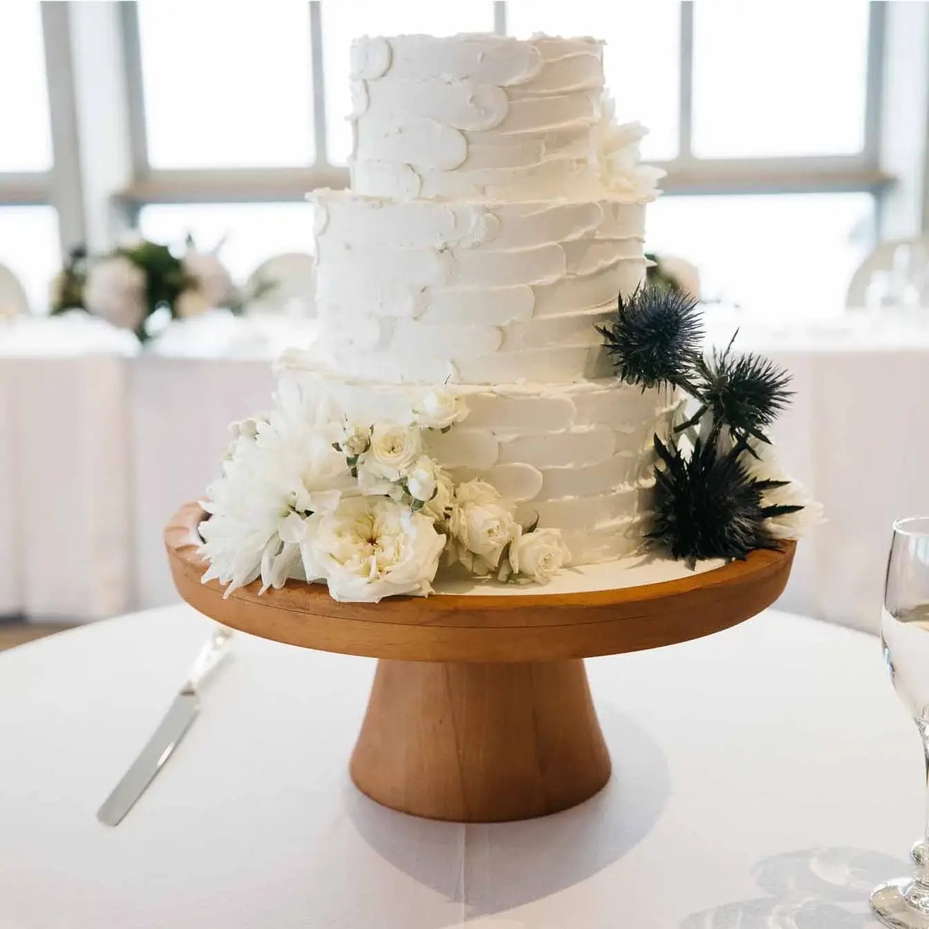 Rustic Coastal Bliss Wedding Cake - A three-tier cake with a rustic palette knife finish and adorned with fresh flowers, a centerpiece that captures the essence of coastal romance