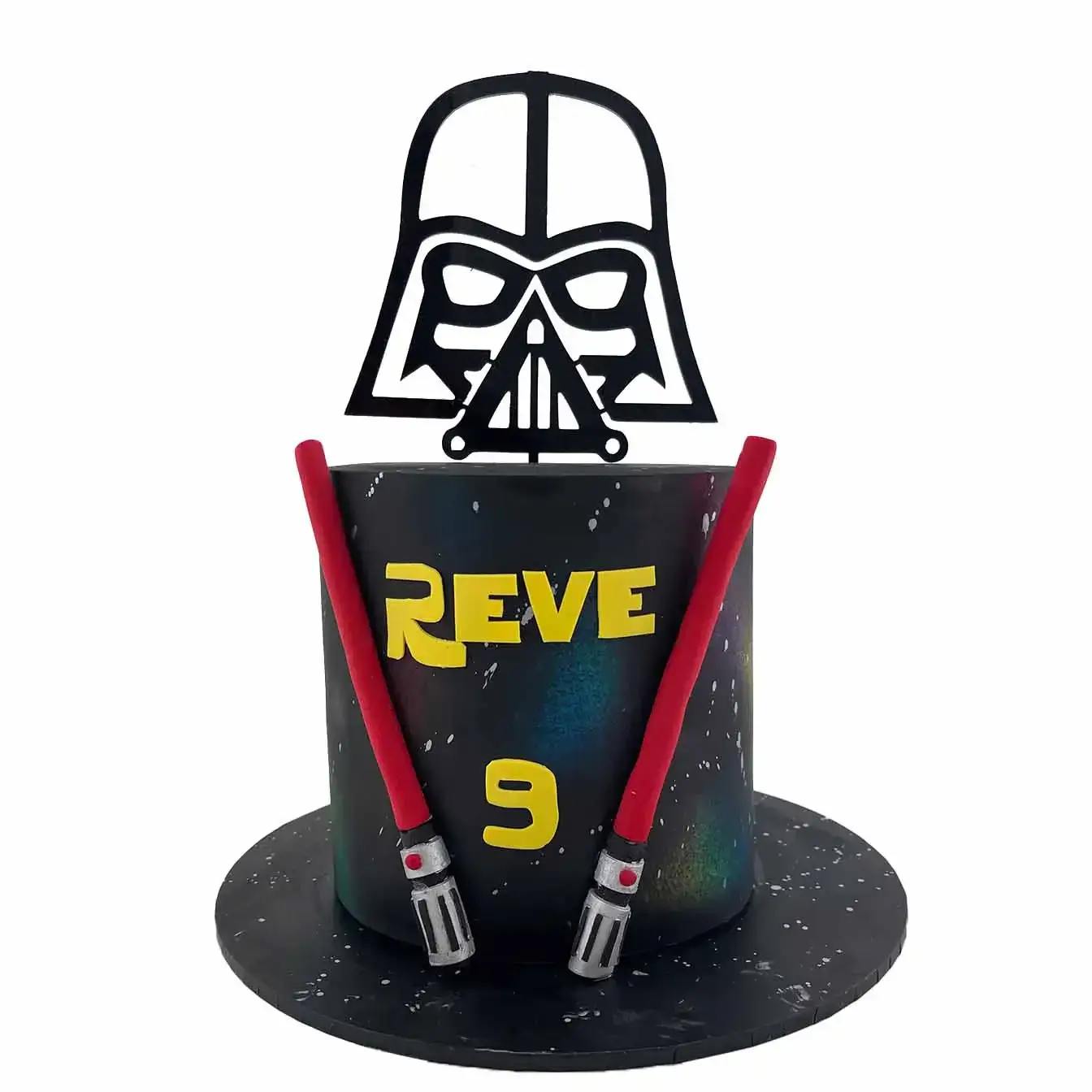 Galactic Jedi Masterpiece Cake - A galaxy fondant-iced cake with two lightsabers and a Darth Vader acrylic cake topper, a captivating centerpiece for Star Wars enthusiasts and space-themed celebrations.